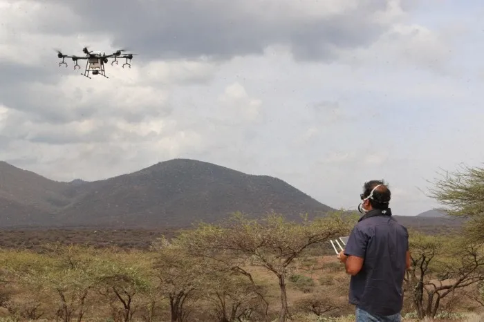 An operator flying a spray drone over scrubland in Samburu