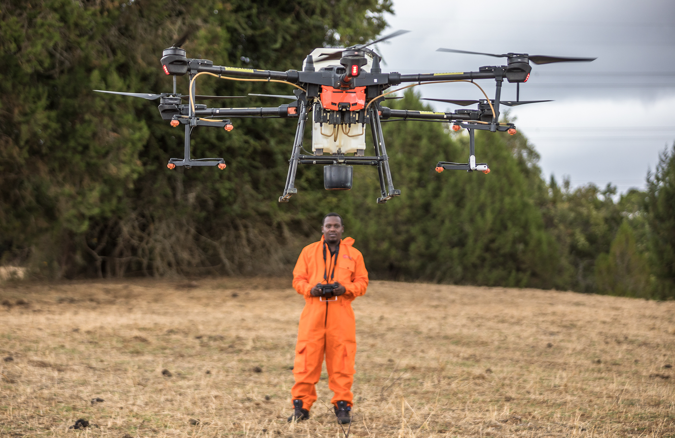 A retrofitted DJI Agras drone in flight above its operator during field testing in Kenya