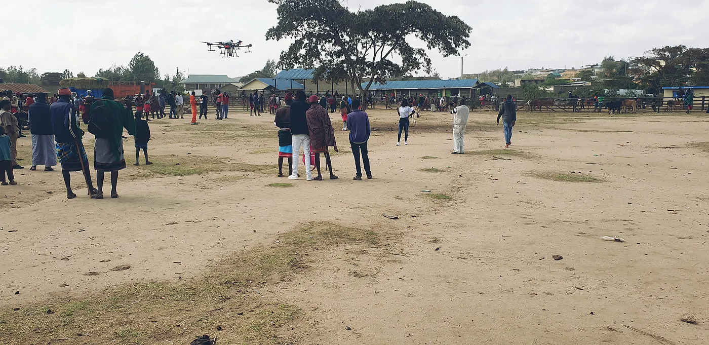 A crowd at a livestock market in Samburu watching a drone spraying demonstration