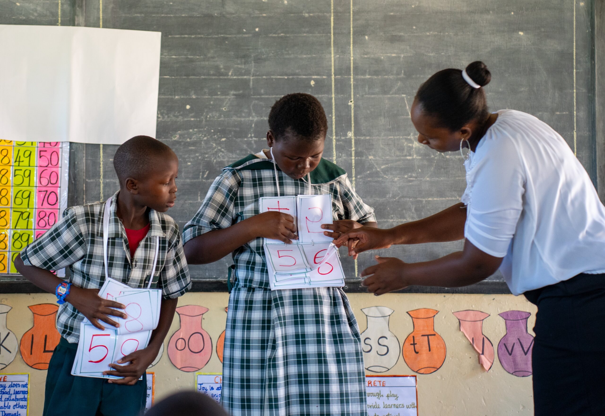A teacher works with two pupils using place-value cards in a Zambian classroom